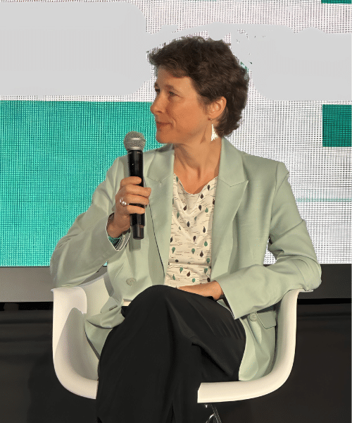 Photo of Miriam Ueberall sitting on an event stage with a microphone.