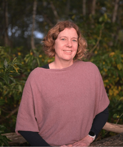 Photo of An Michiels in front of a dark leafy background.