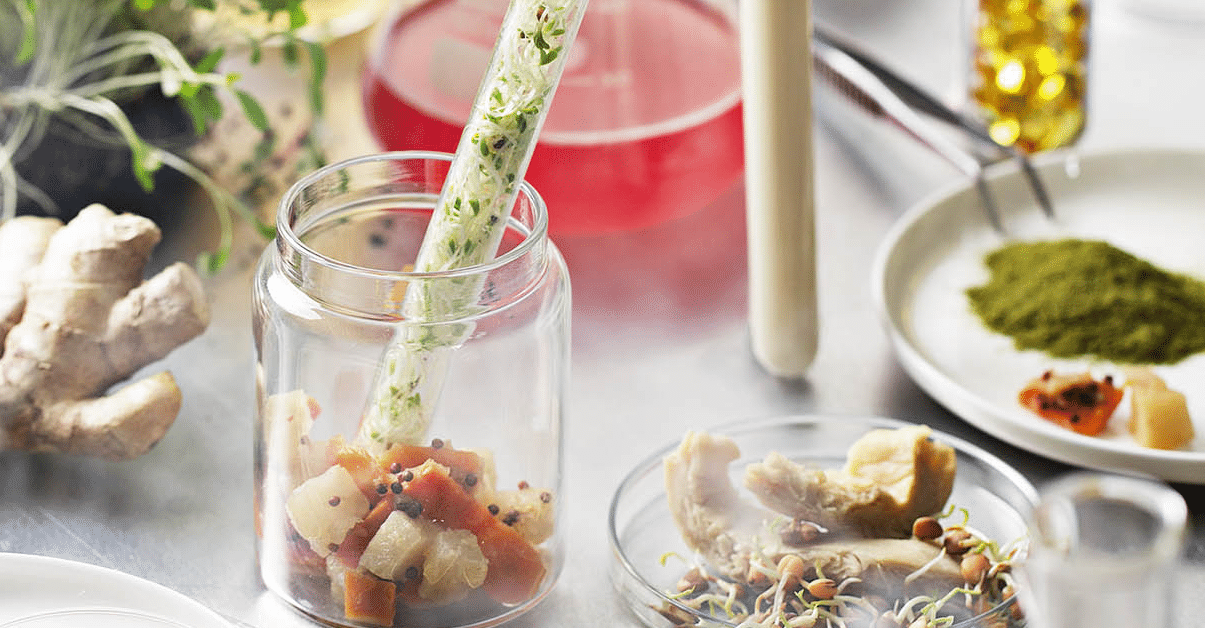 Various food ingredients, including micro-greens, ginger, and mushrooms, displayed in scientific equipment, including test tubes, conical flasks, and petri dishes.