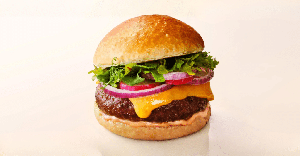 An image of a beef burger with cheese, onion, and lettuce on a plain beige background.